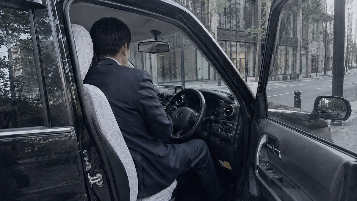 運転席に座り街へ出るジャパンタクシーのドライバーの後ろ姿