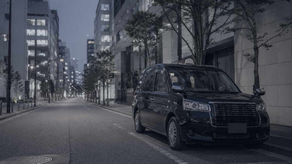 夜のオフィス街の路肩に停まるジャパンタクシー
